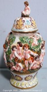 Vintage Porcelain Hand Painted Italian Capodimonte Urn with Lid and Handles with Frolicking Figurals & Cherubs.  Measures approximately 17" tall with lid. 
