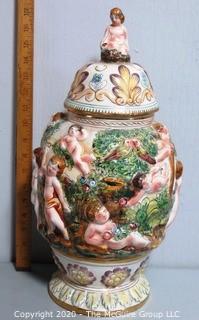 Vintage Porcelain Hand Painted Italian Capodimonte Urn with Lid and Handles with Frolicking Figurals & Cherubs.  Measures approximately 17" tall with lid. 
