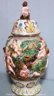 Vintage Porcelain Hand Painted Italian Capodimonte Urn with Lid and Handles with Frolicking Figurals & Cherubs.  Measures approximately 17" tall with lid. 
