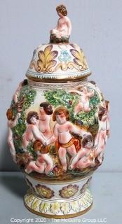 Vintage Porcelain Hand Painted Italian Capodimonte Urn with Lid and Handles with Frolicking Figurals & Cherubs.  Measures approximately 17" tall with lid. 
