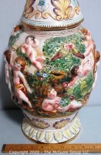 Vintage Porcelain Hand Painted Italian Capodimonte Urn with Lid and Handles with Frolicking Figurals & Cherubs.  Measures approximately 17" tall with lid. 
