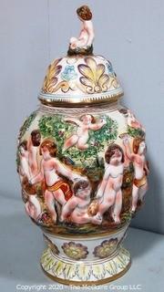 Vintage Porcelain Hand Painted Italian Capodimonte Urn with Lid and Handles with Frolicking Figurals & Cherubs.  Measures approximately 17" tall with lid. 
