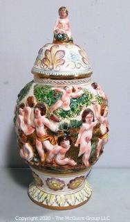 Vintage Porcelain Hand Painted Italian Capodimonte Urn with Lid and Handles with Frolicking Figurals & Cherubs. Several Repairs and chips. Measures approximately 17" tall with lid. 
