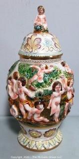 Vintage Porcelain Hand Painted Italian Capodimonte Urn with Lid and Handles with Frolicking Figurals & Cherubs. Several Repairs and chips. Measures approximately 17" tall with lid. 
