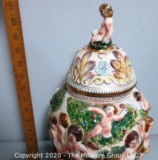 Vintage Porcelain Hand Painted Italian Capodimonte Urn with Lid and Handles with Frolicking Figurals & Cherubs. Several Repairs and chips. Measures approximately 17" tall with lid. 
