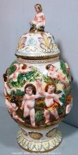 Vintage Porcelain Hand Painted Italian Capodimonte Urn with Lid and Handles with Frolicking Figurals & Cherubs. Several Repairs and chips. Measures approximately 17" tall with lid. 
