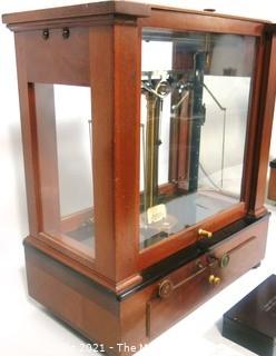 Antique Triple Beam Balance Gold or Apothecary Cabinet Scale in a Glass and Wood Case by Christian Becker, New York.. It has glass panels on all four side and has one drawer with weights and other accessories.   It measures approximately 18" x 16" x 9".