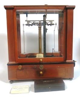 Antique Triple Beam Balance Gold or Apothecary Cabinet Scale in a Glass and Wood Case by Christian Becker, New York.. It has glass panels on all four side and has one drawer with weights and other accessories.   It measures approximately 18" x 16" x 9".