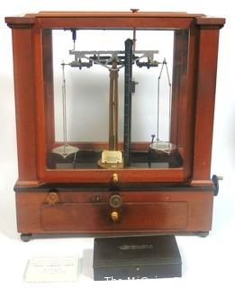 Antique Triple Beam Balance Gold or Apothecary Cabinet Scale in a Glass and Wood Case by Christian Becker, New York.. It has glass panels on all four side and has one drawer with weights and other accessories.   It measures approximately 18" x 16" x 9".