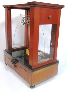 Antique Triple Beam Balance Gold or Apothecary Cabinet Scale in a Glass and Wood Case Made by Voland & Sons of New Rochelle, NY, 1912. It has glass panels on all four side and has one drawer with box of scale weights. It measures approximately 21" x 16" x 9".