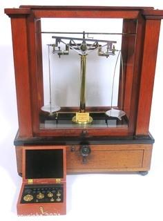 Antique Triple Beam Balance Gold or Apothecary Cabinet Scale in a Glass and Wood Case Made by Voland & Sons of New Rochelle, NY, 1912. It has glass panels on all four side and has one drawer with box of scale weights. It measures approximately 21" x 16" x 9".