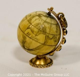 Antique Scrimshaw Articulated Globe Charm or Pendant in 14kt Gold Stand with Raw Sapphire Decorative Gemstones. It measures approximately 1 1/4" tall and weights 10.7g.