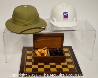 Collection including chess board with wooden pieces, Pentagon Renovation Program Hard Hat and Singaporean Field Hard Hat.  