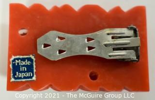 Molded Red Celluloid or Bakelite Clip, Made in Japan. It measures approximately 2" long and 1 1/4" wide.